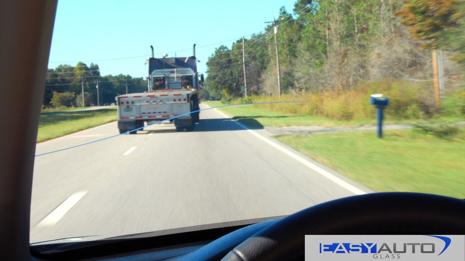 A cracked windshield on a car, driving behind a semi-truck.
